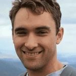 a man smiling with a mountain in the background.