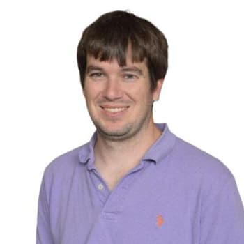 a man in a purple shirt smiling at the camera.