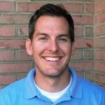 a man smiling in front of a brick wall.