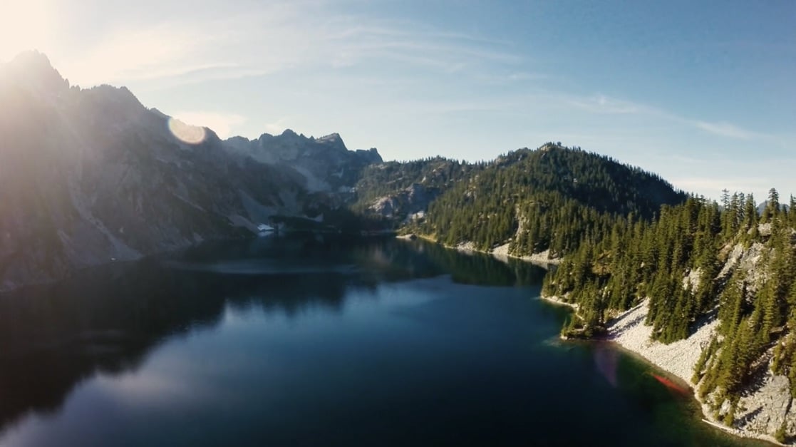 a lake surrounded by mountains and trees on a sunny day.